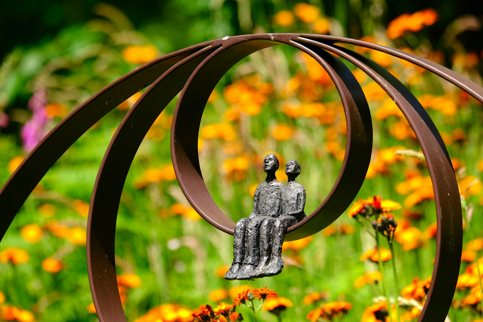 Metalen element met sculptuur van twee zittende figuren, omringd door oranje bloemen