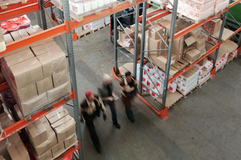 Drie medewerkers lopen langs stellingen met kunststof pallets vol dozen in een actief magazijn